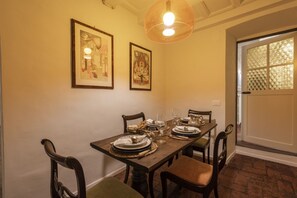 A dining room with a wooden table set for four, framed artwork on the wall, and a hanging light fixture.