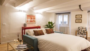 Un dormitorio con cama, mesita de noche, silla, ventana y radiador.