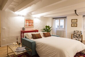 A bedroom with a bed, a side table, a chair, a window, and a radiator.