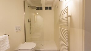Un baño pequeño y moderno con inodoro, cabina de ducha con mampara de vidrio y una toalla blanca colgada en la pared.