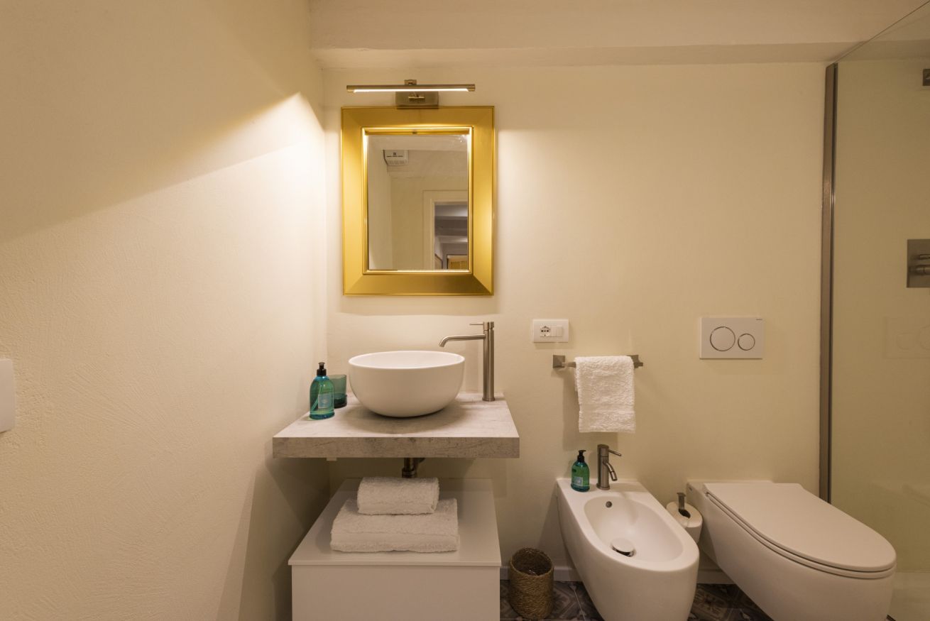 A bathroom with a white sink, a mirror with a gold frame, a bidet, and a toilet.