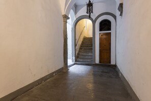 A hallway with a wooden door at the end, a staircase, and a hanging light fixture.
