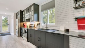 A modern kitchen with dark cabinets, a stainless steel refrigerator, and a window providing a view of the outdoors. - Lakefront Catskills Container Home: Private Lake (Swan Lake)