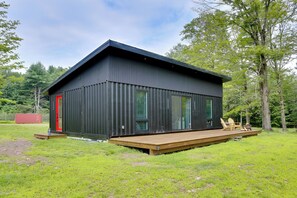 A modern black building with a red door, large windows, and a wooden deck. - Lakefront Catskills Container Home: Private Lake (Swan Lake)