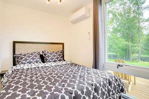 A bedroom with a bed, a window with a view of trees, and an air conditioning unit on the wall. - Lakefront Catskills Container Home: Private Lake (Swan Lake)