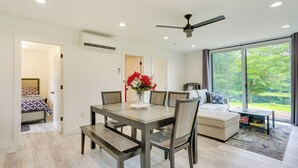 A modern living room with a dining table, chairs, and a sofa. There is a large window with a view of greenery outside. - Lakefront Catskills Container Home: Private Lake (Swan Lake)