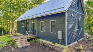 Une petite cabane à un seul étage, dotée d’un toit en pente, d’un porche en bois et d’une petite terrasse.