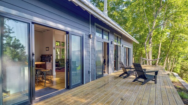 Une maison moderne dotée d’une terrasse, de portes-fenêtres coulissantes et offrant une vue sur les arbres environnants.