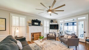 A spacious living room with a fireplace, a ceiling fan, and a large window offering a view of the outdoors. - Waterfront Vacation Property on the Pamlico (Bath)