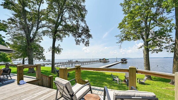 A wooden deck with outdoor seating, overlooking a lake with a dock and pier. - Waterfront Vacation Property on the Pamlico (Bath)