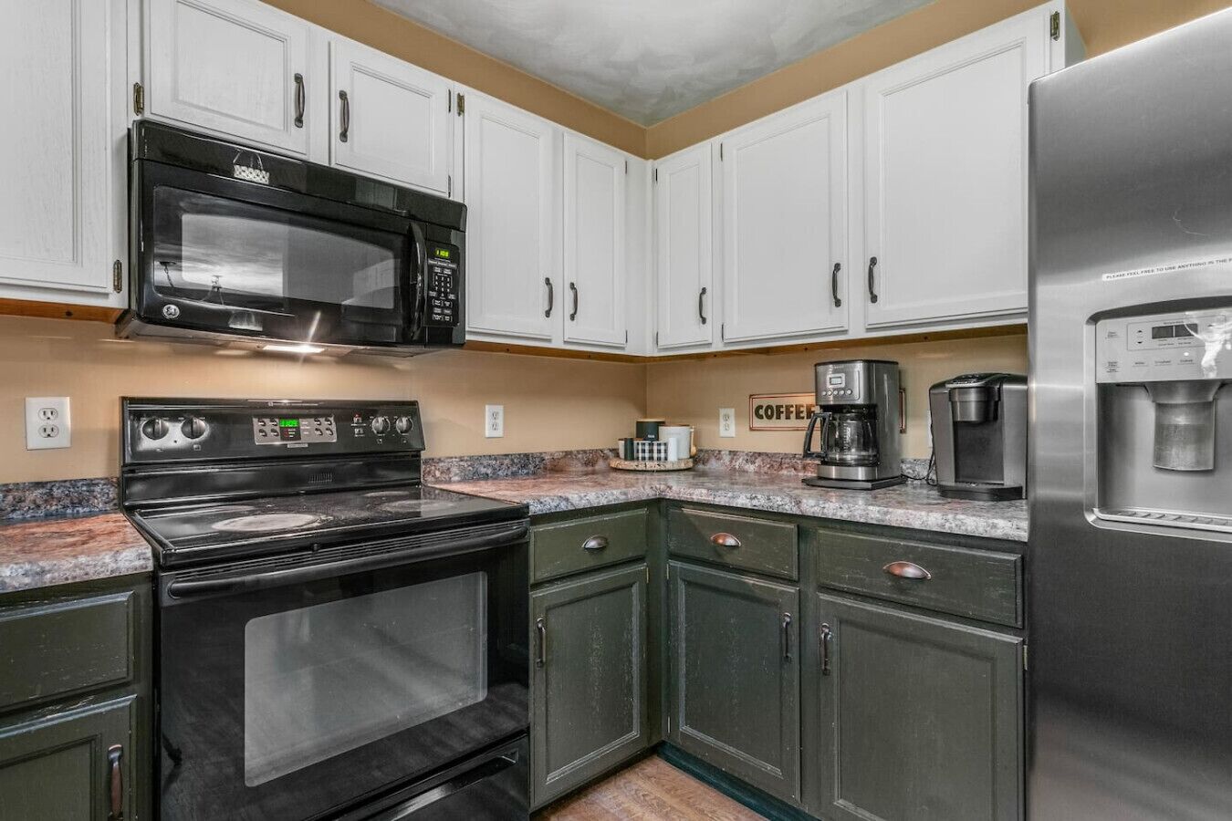 A kitchen with white cabinets, a black stove, a microwave, a coffee maker, and a refrigerator.