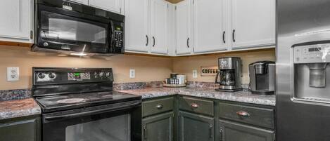 A kitchen with white cabinets, a black stove, a microwave, a coffee maker, and a refrigerator.