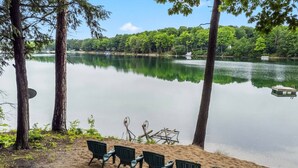 Une vue sur le lac, avec une rangée de chaises disposées face à l’eau, entourées d’arbres et d’une jetée.