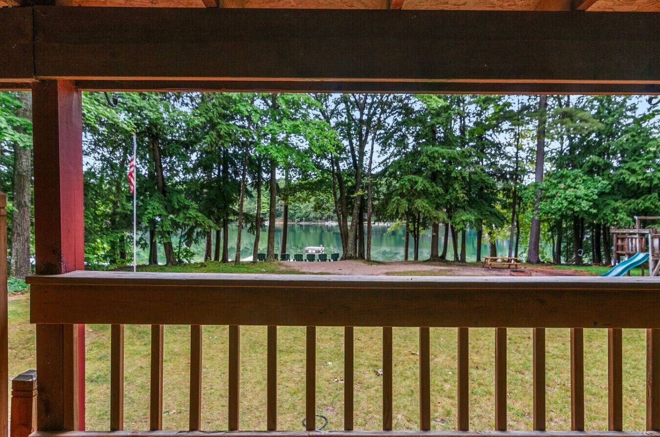 Una terraza de madera con vistas a un parque, que incluye árboles y un área de juegos.