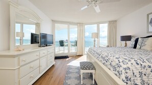 A bedroom with a large bed, a TV, a dresser, and a view of the ocean through the sliding glass doors. - OE at White Surf Unit 306 (Daytona Beach Shores)