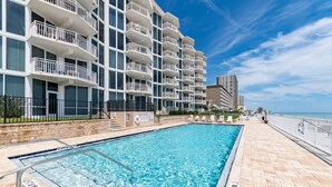 A swimming pool adjacent to a multi-story hotel with balconies, a beach view, and a lifeguard tower. - OE at White Surf Unit 306 (Daytona Beach Shores)