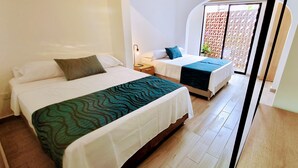 Ein Hotelzimmer mit zwei Betten, jeweils mit weißer Bettdecke und grüner, gemusterter Decke. Dazwischen steht ein Nachttisch mit einer Lampe.