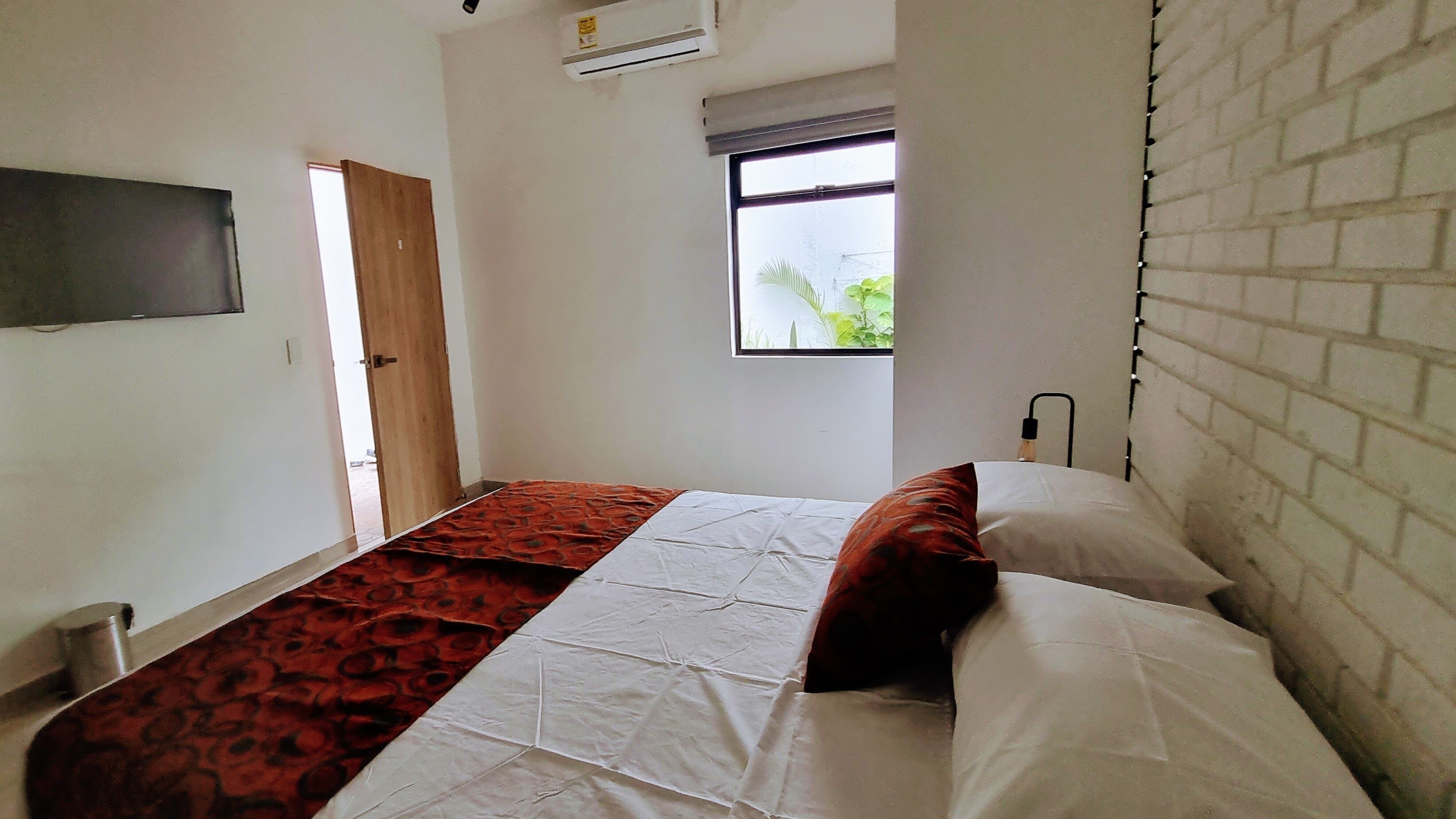 A bedroom with a bed, a window, a door, and a wall-mounted air conditioner.