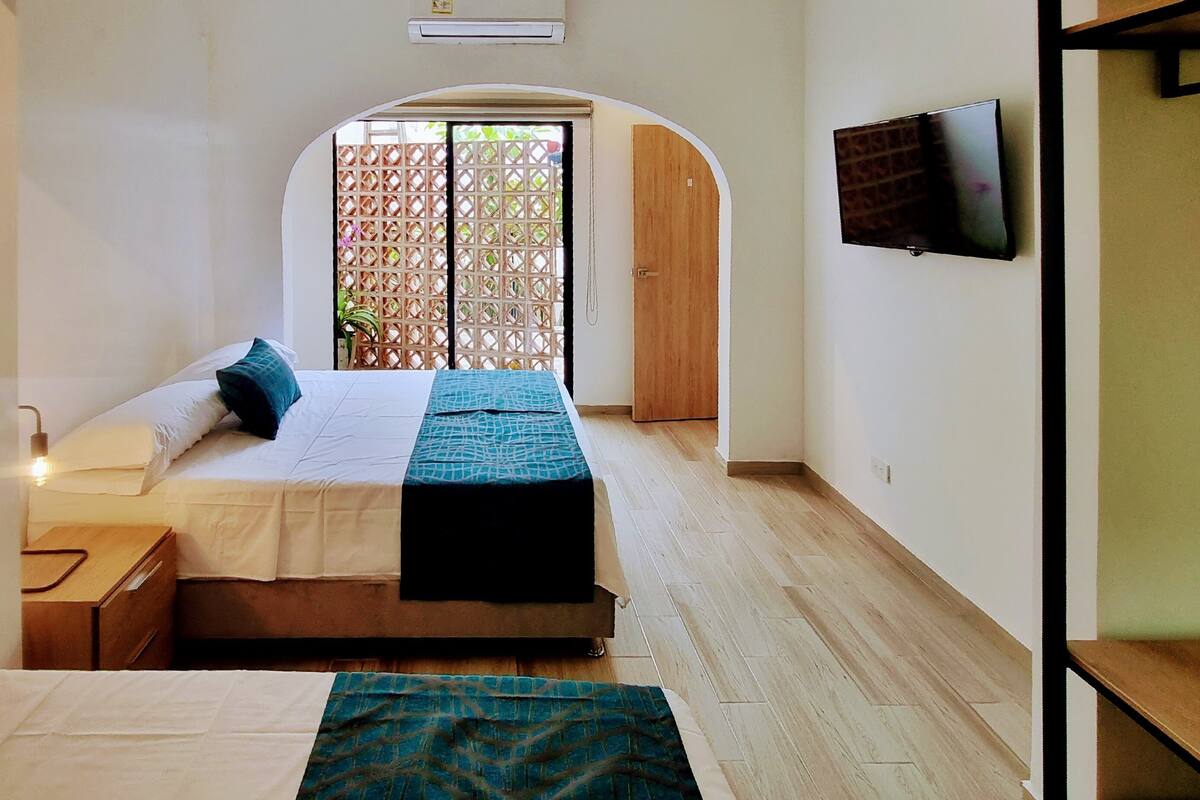 A hotel room with a bed, a desk, a TV, and a view through an arched doorway.