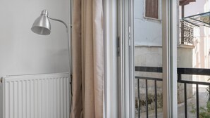 Een kamer met een radiator, een raam met gordijnen en een balkon met een metalen hekwerk.