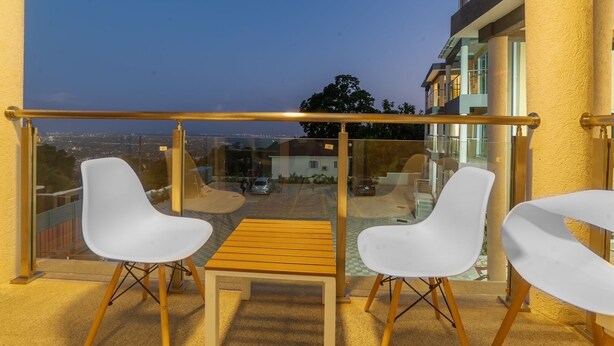 A balcony with two white chairs and a small wooden table, overlooking a cityscape at dusk. - Hibiscus Charm - 2BR-2BA w/Pool (Kingston)