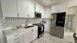 A modern kitchen with white cabinets, a stainless steel refrigerator, a microwave, and a tiled backsplash. - Hibiscus Charm - 2BR-2BA w/Pool (Kingston)