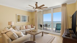 Een woonkamer met een bank, salontafel en plafondventilator. Er is een balkon met uitzicht op de oceaan.