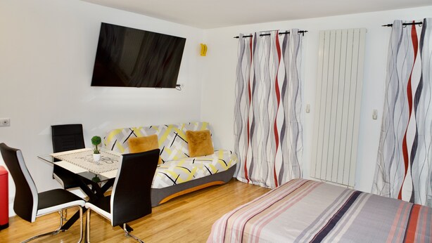 A modern bedroom with a bed, a sofa, a TV, and a dining area with chairs and a table. - Studio Jasmin (Paris)