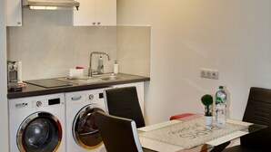 A compact kitchen with a washing machine, a sink, and a table with chairs. - Studio Jasmin (Paris)