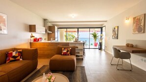 A modern living room with a sofa, coffee table, and a dining area with a bar. There is a view of the ocean through large windows. - Florida Sun : Beautiful appartment with sea view (Schoelcher)