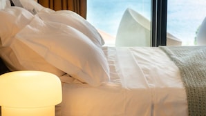 A neatly made bed with white linens and pillows, a bedside lamp, and a view of the sky through a window. - Florida Sun : Beautiful appartment with sea view (Schoelcher)