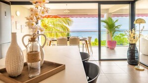 A modern dining area with a view of the ocean, featuring a table set for two, a potted plant, and a vase with flowers. - Florida Sun : Beautiful appartment with sea view (Schoelcher)