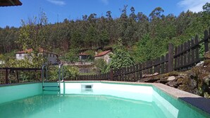 En rektangulär swimmingpool med en metallstege, omgiven av ett trästaket och en stenmur.