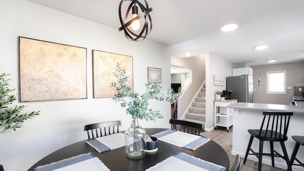Una cocina moderna con una isla central, un área de comedor con una mesa redonda y una escalera que lleva a un nivel superior.