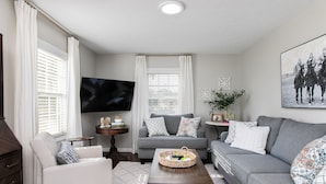 Una sala de estar con un sofá gris, un sillón blanco y una mesa de centro con una cesta.
