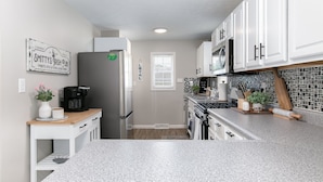 Una cocina moderna con armarios blancos, encimera de granito, refrigerador de acero inoxidable y cafetera.