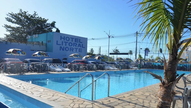 A hotel pool area with lounge chairs and umbrellas, a clear blue sky, and a palm tree. - No property  (Centro Caraguatatuba)