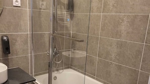 A modern bathroom with a glass-enclosed shower, a white bathtub, and a black countertop with a sink. - Appartement Proche de Vernon Giverny (Vernon)