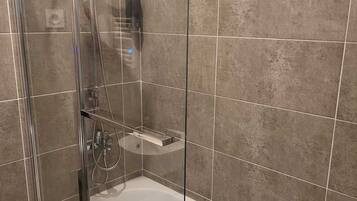 A modern bathroom with a glass-enclosed shower, a white bathtub, and a handheld showerhead.
