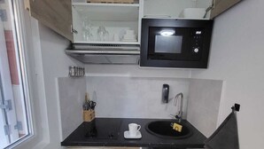 Cocina compacta con microondas, fregadero y armarios de madera.