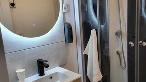 Un baño moderno con ducha de vidrio, lavamanos blanco y un espejo grande.