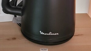 Una tetera eléctrica negra con asa y pico, con el rótulo 'Moulinex', sobre una superficie de madera.