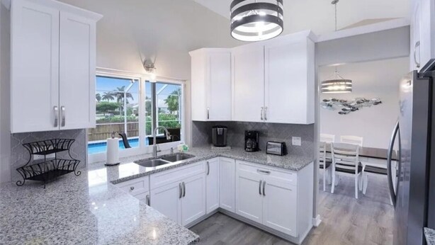 A modern kitchen with white cabinets, granite countertops, and a built-in island. There is a dining area with a white table and chairs, and a view of a swimming pool. - Tropical Vacation Home Marco Island Florida - Close to Beaches-Pet Friendly-POOL (Marco Island)