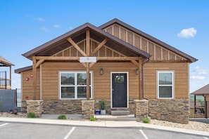 Two-story building with a gabled roof and central wooden beam design, featuring a black front door and two windows with white frames.