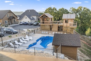 A residential area with a swimming pool, lounge chairs, and a wooden playhouse.