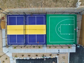 Una cancha de baloncesto al aire libre con aro, rodeada por una valla y un camino pavimentado.