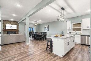 A modern kitchen with white cabinets, a stainless steel refrigerator, and a dining area with a table and chairs. - Near Indoor & Outdoor Pools: Hot Tub, Game Room & Free Silver Dollar City Tickets (Kimberling City)