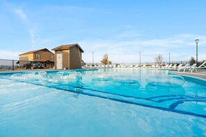 Une piscine avec des chaises longues, un bâtiment doté d’un garage et un ciel dégagé.