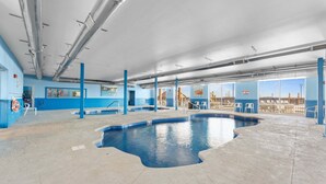Une piscine intérieure à l’eau d’un bleu cristallin, entourée de murs et de piliers bleus, et offrant une vue sur le paysage urbain à travers de grandes fenêtres.