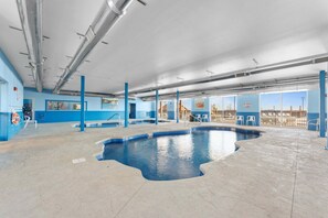 An indoor swimming pool with clear blue water, surrounded by blue walls and pillars, and a view of the cityscape through large windows. - Near Indoor & Outdoor Pools: Hot Tub, Game Room & Free Silver Dollar City Tickets (Kimberling City)